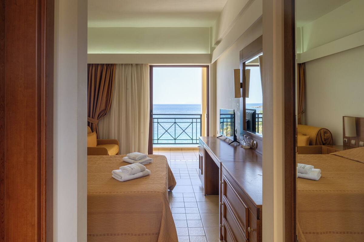 Habitación de hotel con balcón, cama, televisor y cómoda.