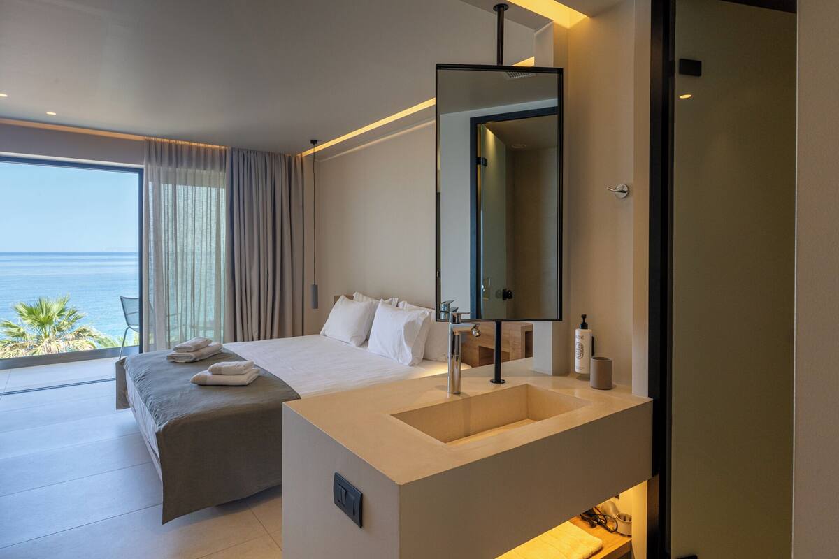 Una habitación de hotel moderna con una cama grande, un lavamanos integrado y vistas al océano.