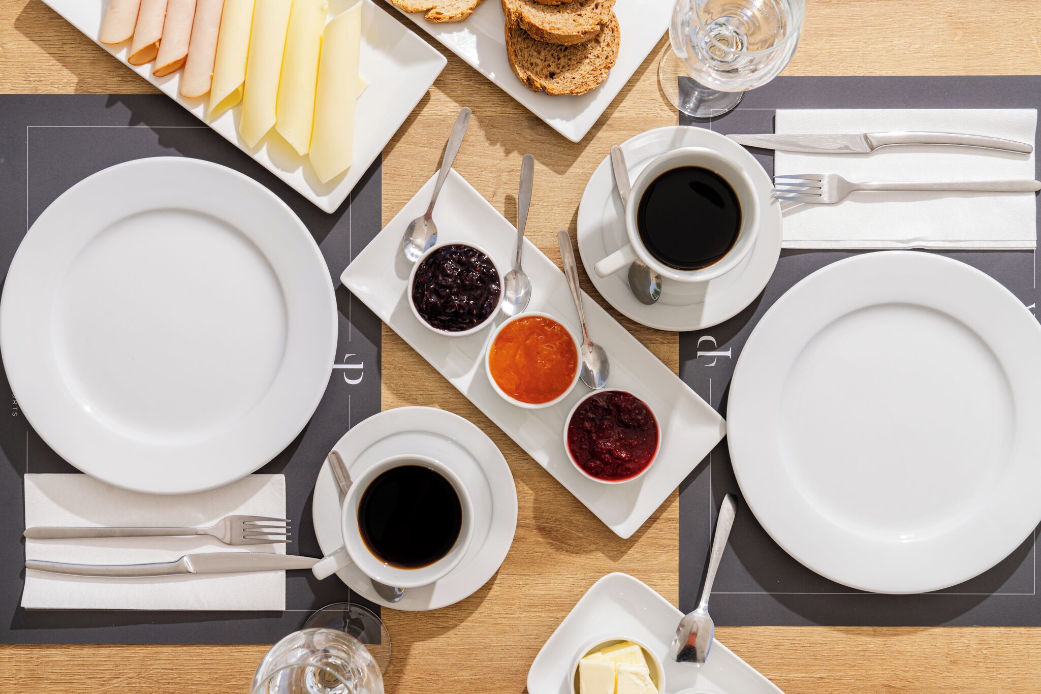 Una mesa de desayuno con platos, tazas de café y diferentes conservas.