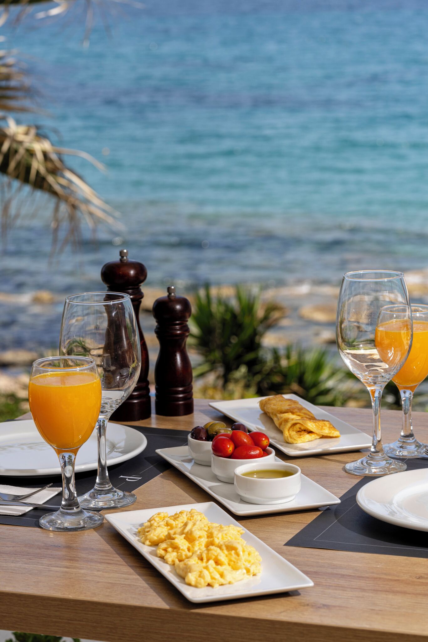 Una mesa de desayuno con huevos revueltos, tostadas y fruta, con vistas panorámicas al océano.