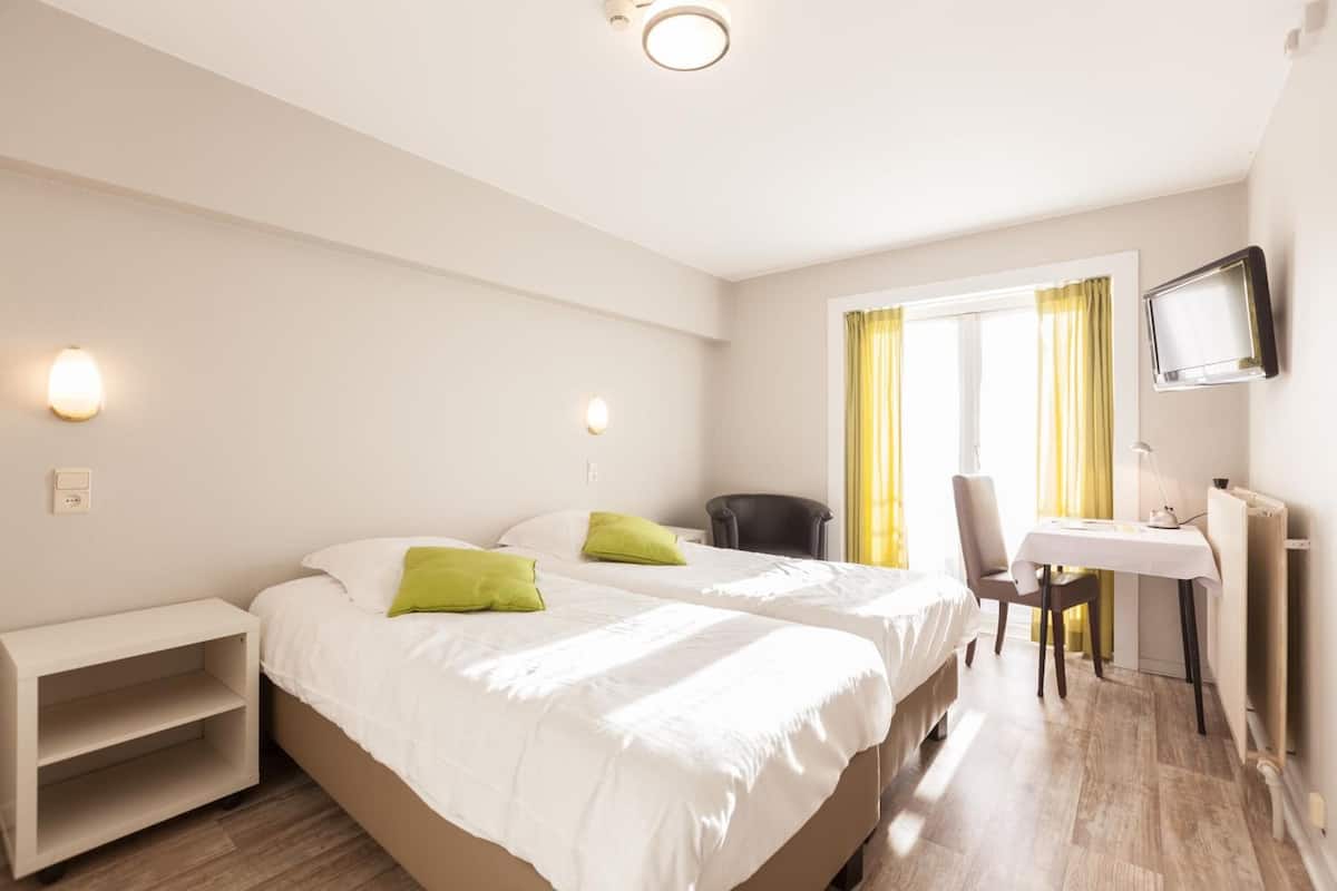 A hotel room with two beds, a desk, a chair, a TV, and a window with curtains.