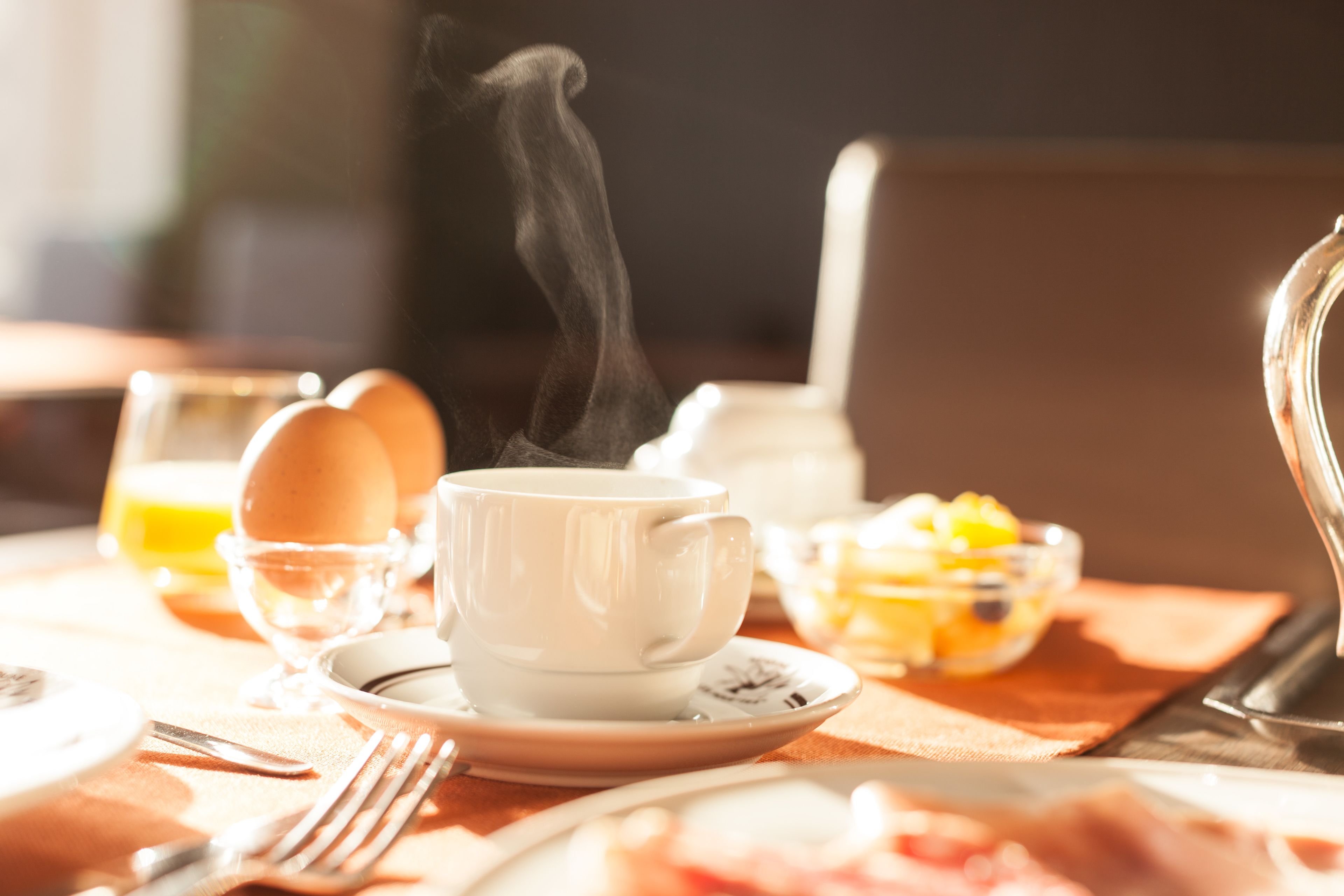 Une table mise pour le petit-déjeuner, avec une tasse de boisson chaude, des œufs et des fruits.