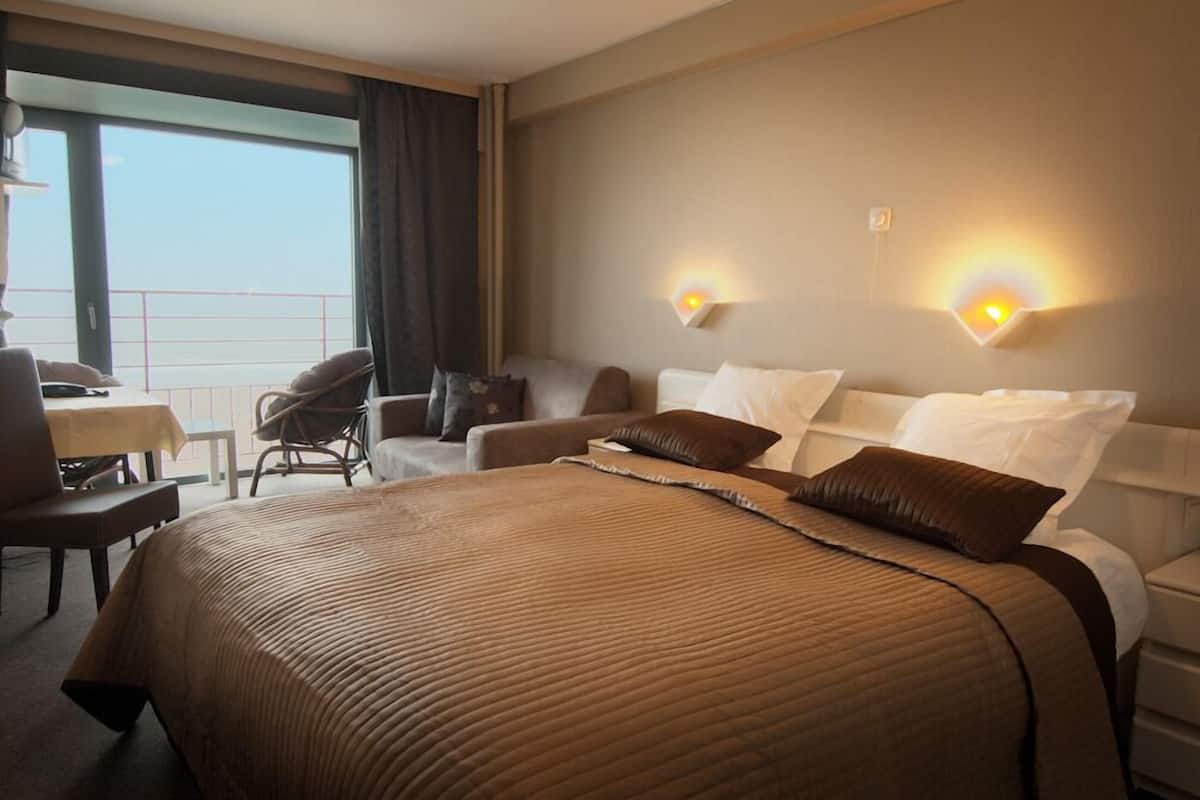 A hotel room with a large bed, a desk, a chair, and a balcony with a view.