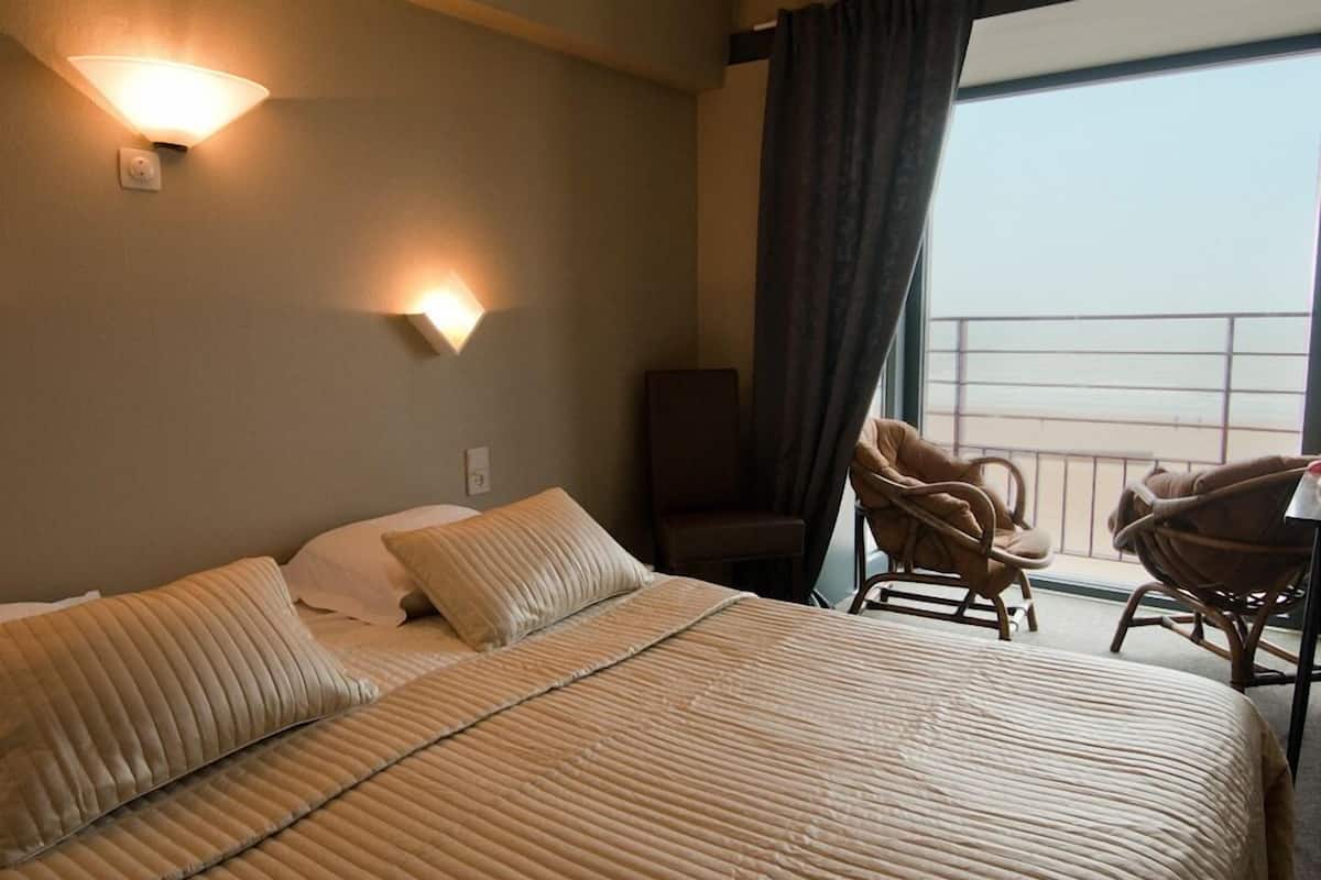 A hotel room with a large bed, two wall-mounted lights, a chair, and a view of the balcony.