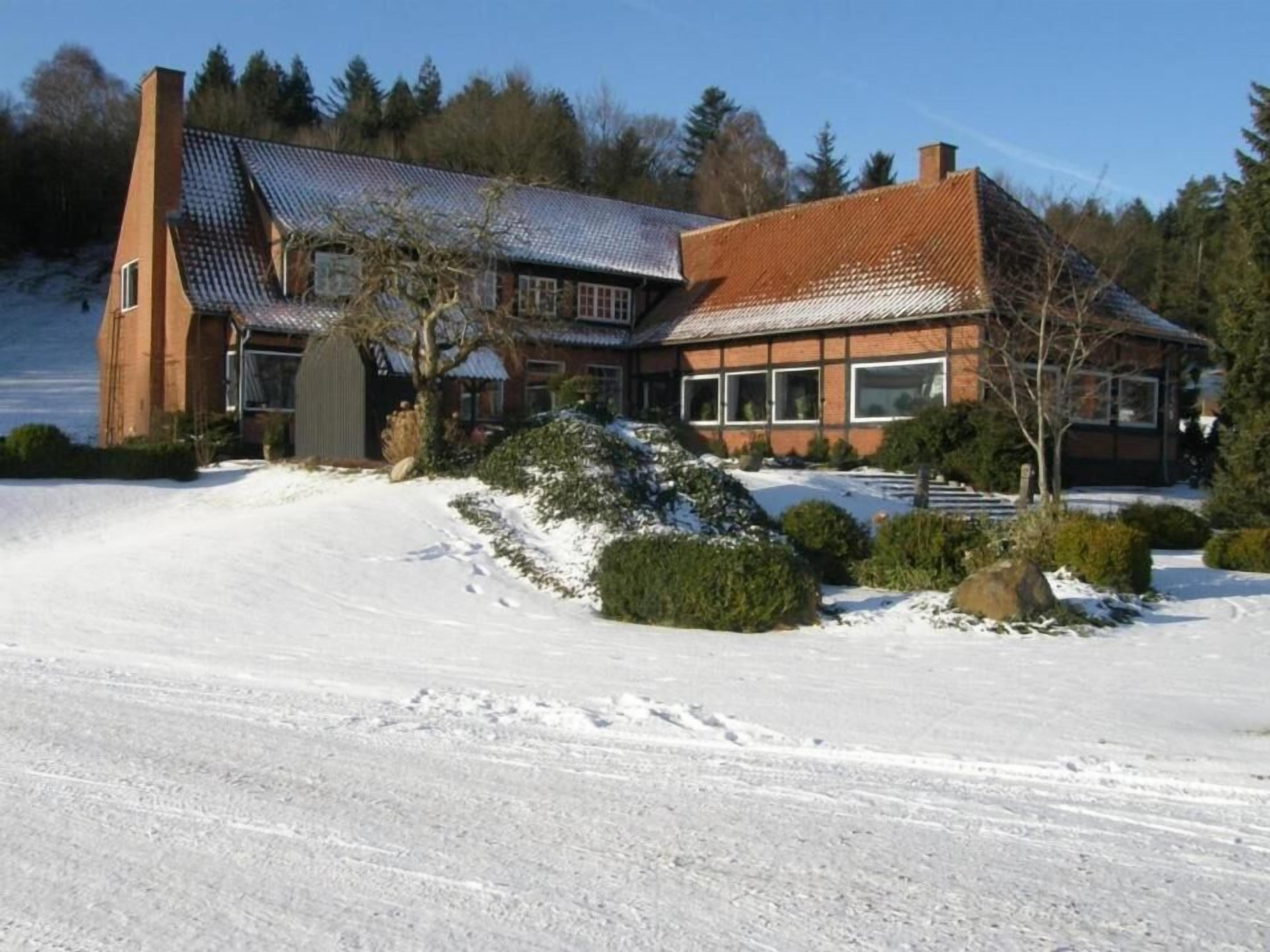 Ett stort, modernt hus med ett sluttande tak, omgivet av snötäckt mark och träd.
