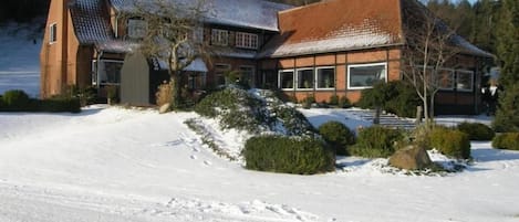 Ett stort, modernt hus med ett sluttande tak, omgivet av snötäckt mark och träd.