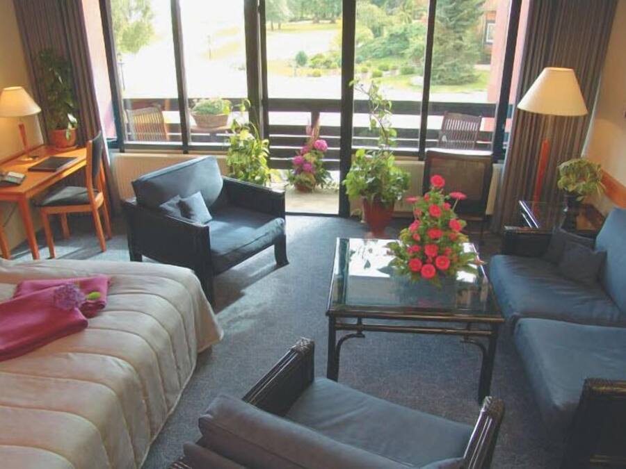 Hotelkamer met een bank, een fauteuil, een bijzettafeltje met bloemen en uitzicht op het landschap door grote ramen.
