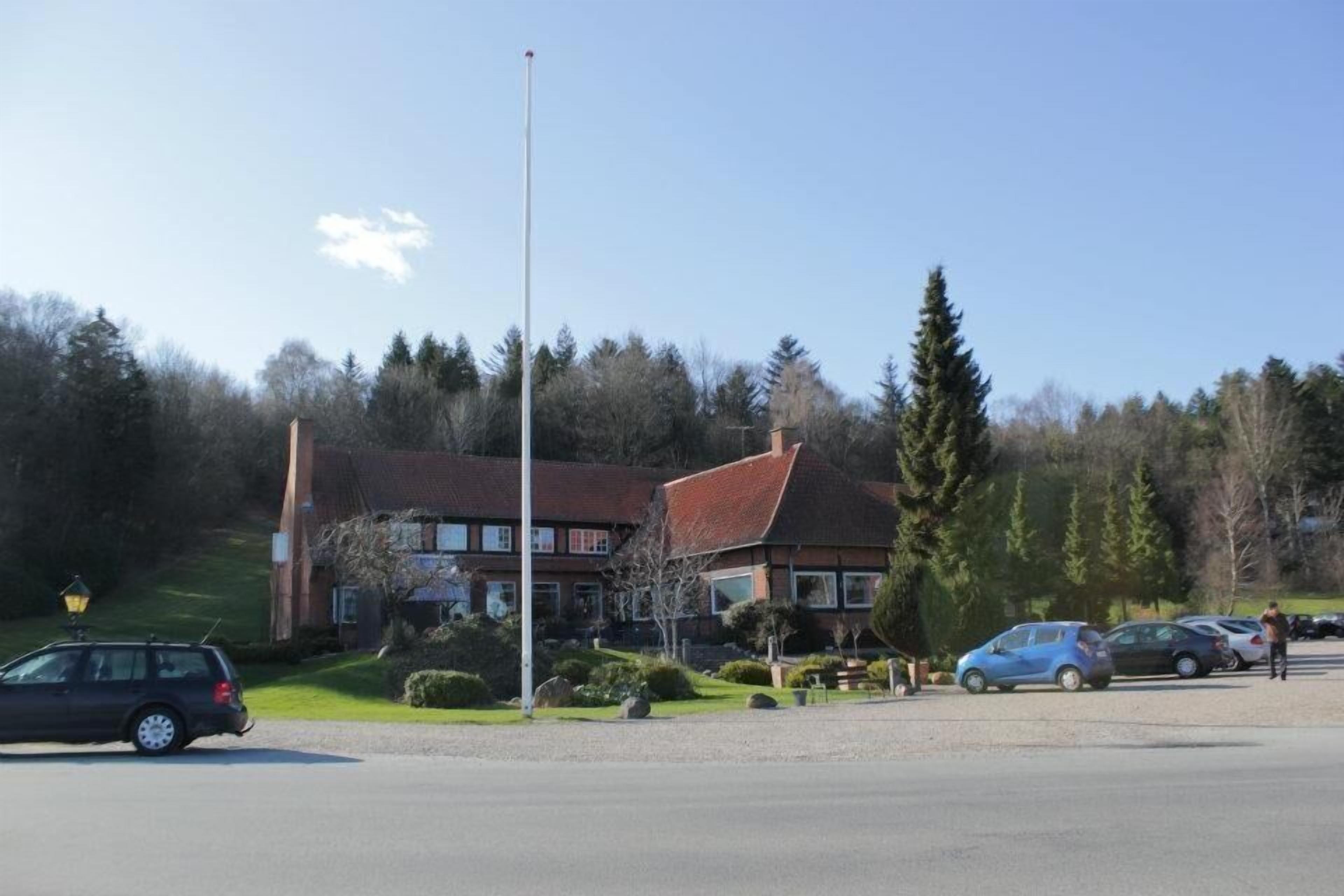 A building with a red roof, surrounded by trees and parked cars.