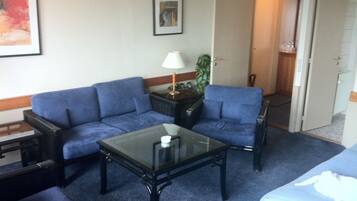 Ein Hotelzimmer mit blauem Sofagarnitur, einem Glastisch, einer Lampe und einer Tür zu einem Badezimmer.