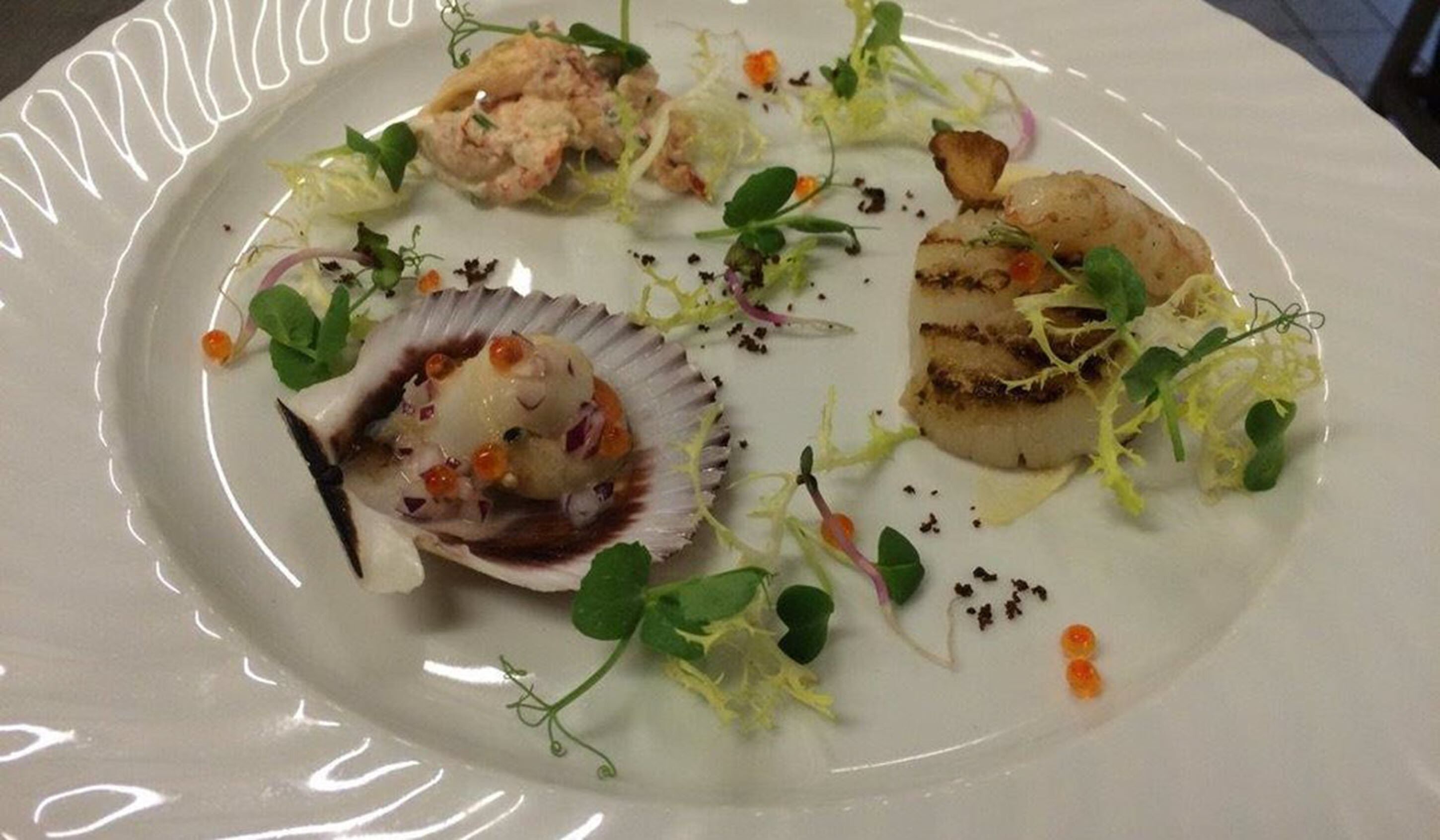 Un plato de comida con diversos guisos, incluyendo vieiras, una concha de vieira y adornos.