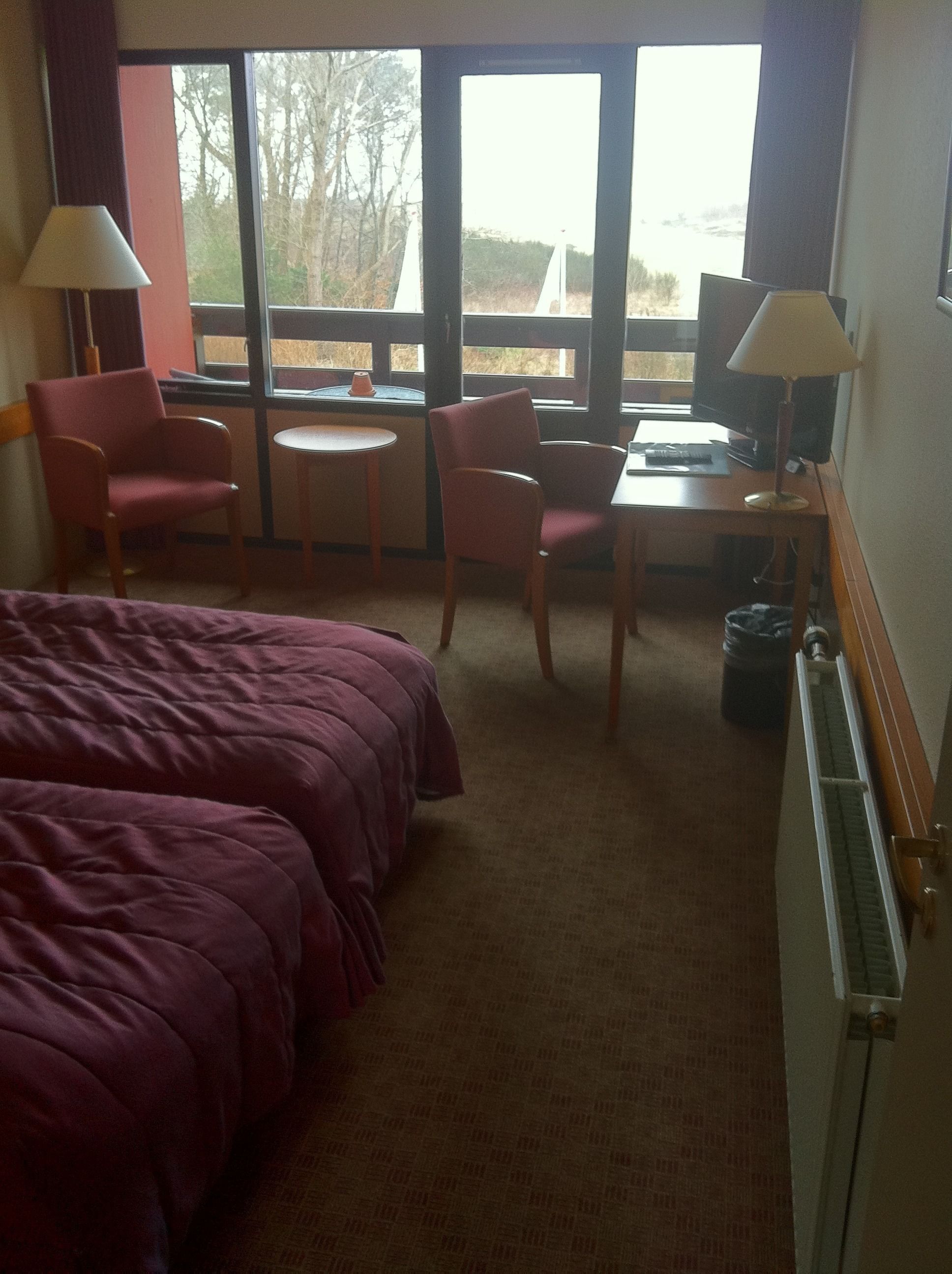 Une chambre d’hôtel comprenant un lit, deux chaises, une petite table, un bureau avec un ordinateur et une vue sur l’extérieur.