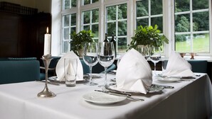 Mesa lista para comer con mantel blanco, cubiertos, copas de vino y una vela.