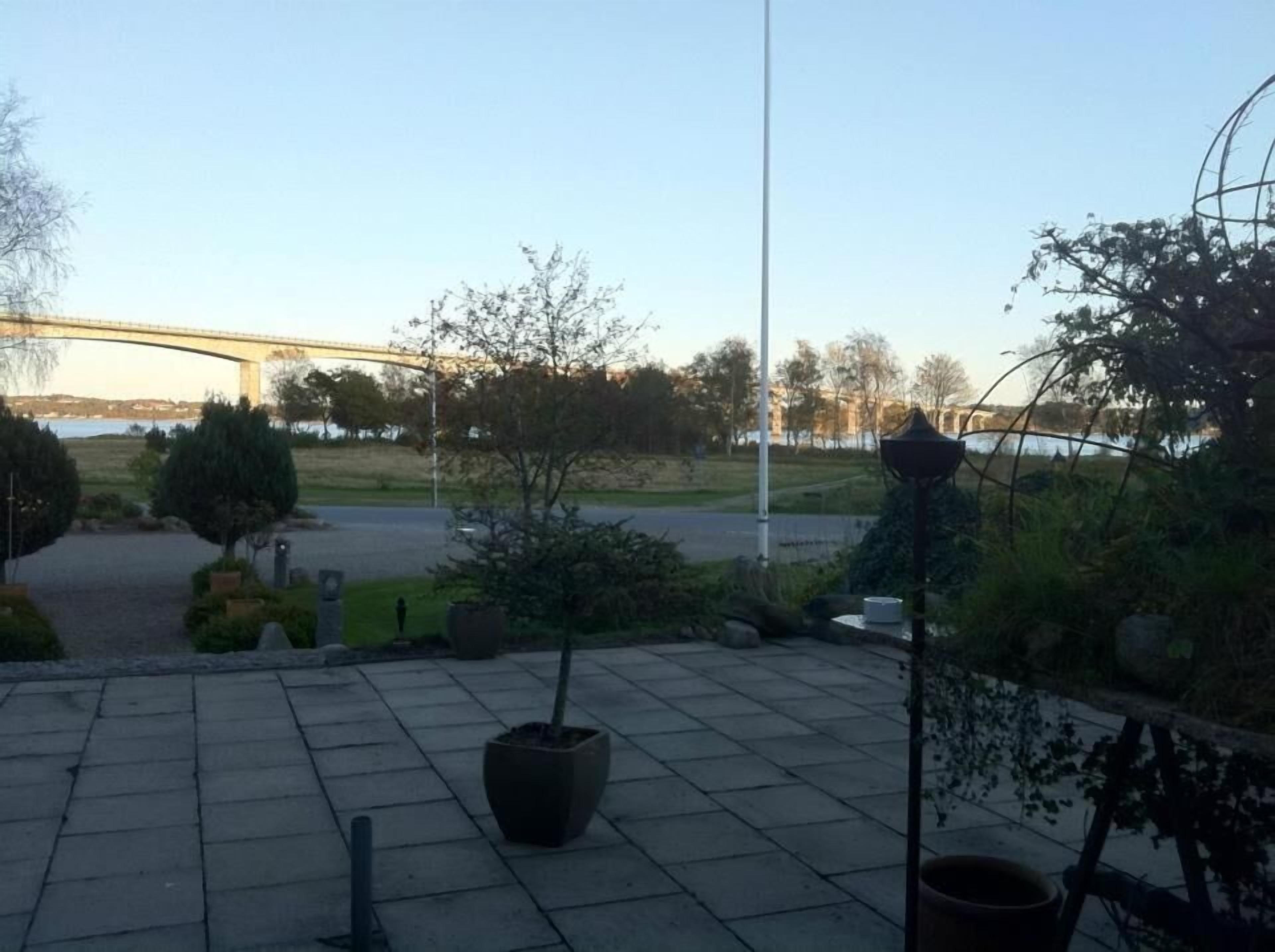 En anlagt udendørs plads med en bro i baggrunden, plantekasser og en lygtepæl.