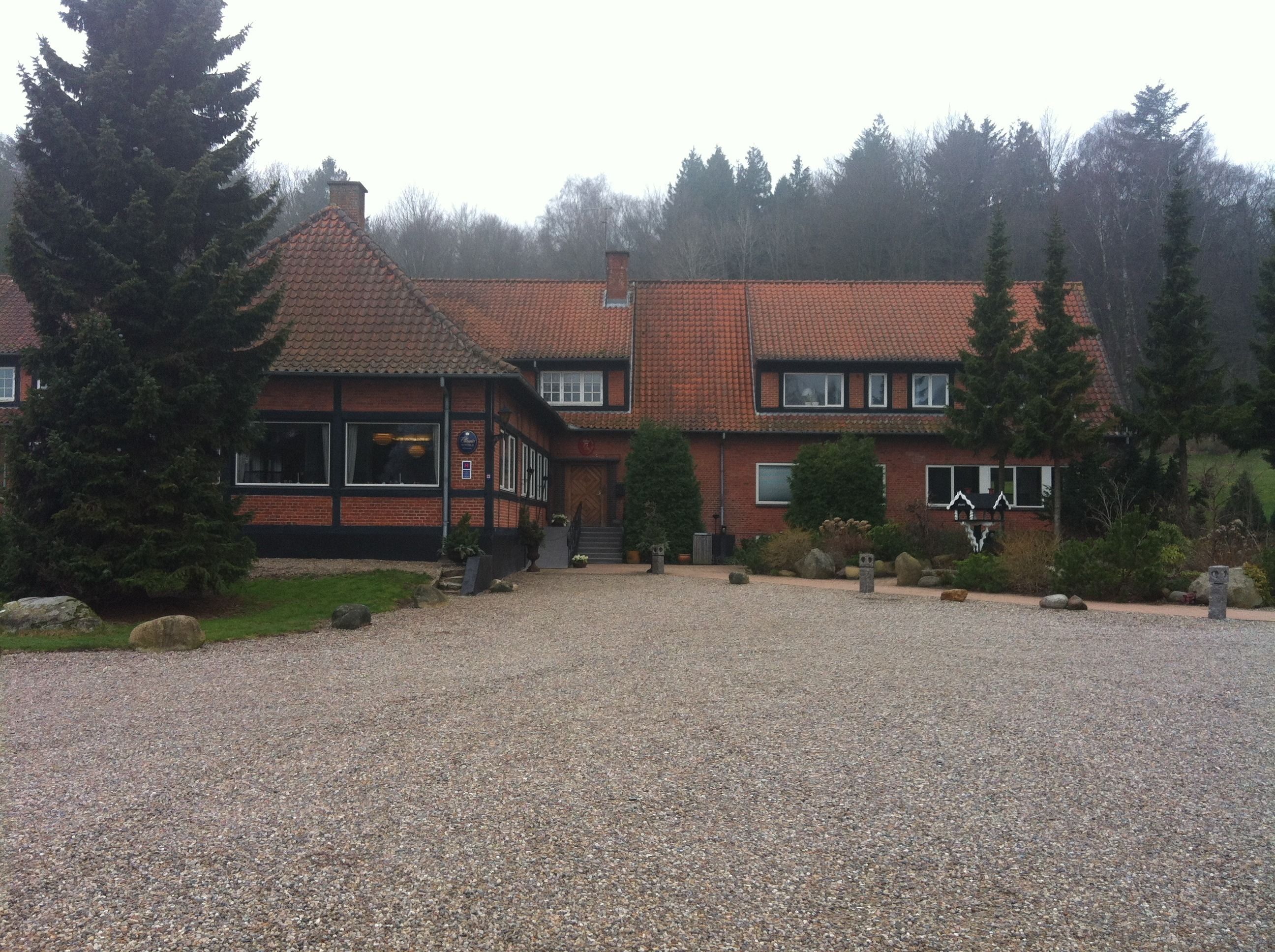 A traditional building with a tiled roof, a gravel driveway, and surrounding greenery.