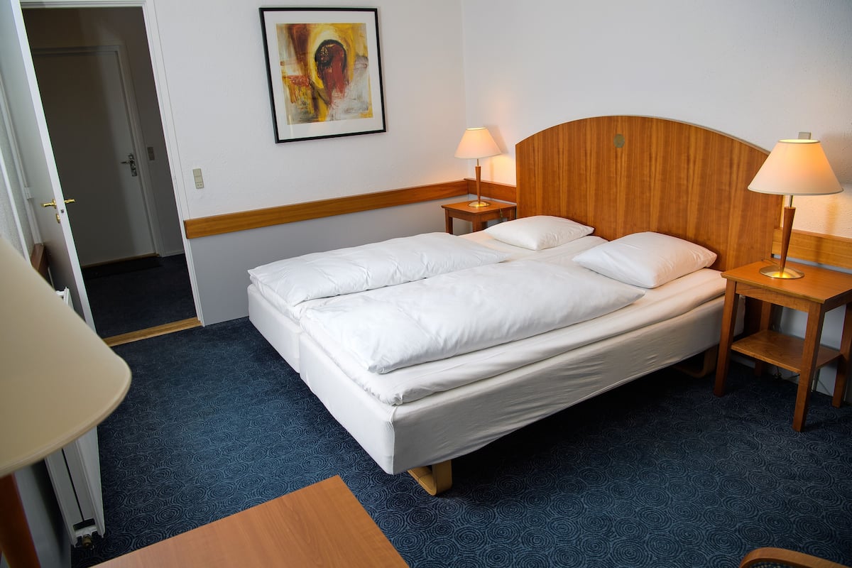 Une chambre d’hôtel avec un lit double, deux tables de chevet avec des lampes, une œuvre d’art encadrée au mur et un sol recouvert de moquette.