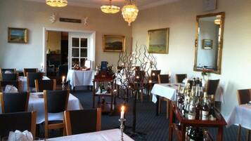 A dining area with tables set for service, a chandelier, and a mirror on the wall.