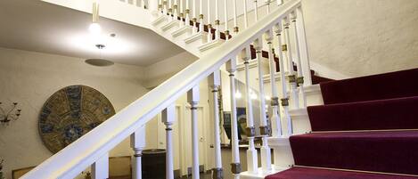 Un magnifique escalier, doté de rampes blanches et de marches recouvertes d’une moquette rouge, mène à l’étage supérieur.