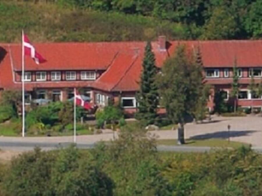 A two-story building with a red roof, multiple windows, and a flagpole with flags.