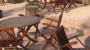 Un área de patio al aire libre con mobiliario de madera, incluyendo una mesa redonda y sillas, y un sendero de piedra.