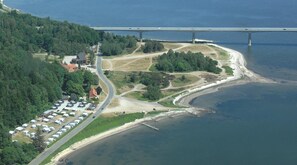 An aerial view of a coastal area with a road leading to a parking lot with RVs, a bridge in the background, and a beach with a pier. - Sallingsund Færgekro (Nykobing Mors)