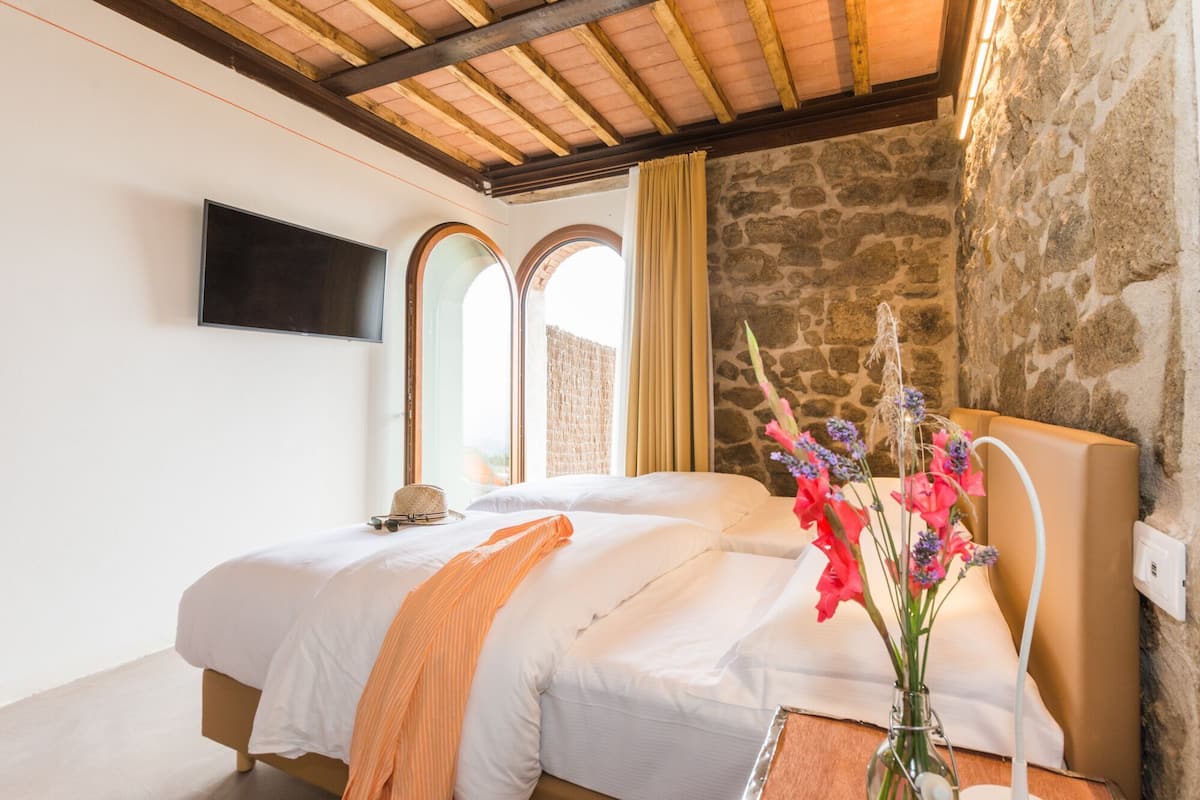 Un dormitorio con cama, televisor, pared de piedra y ventana.