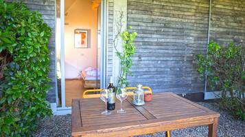 A wooden table with a bottle and glasses on it, placed outside a building with a wooden exterior.