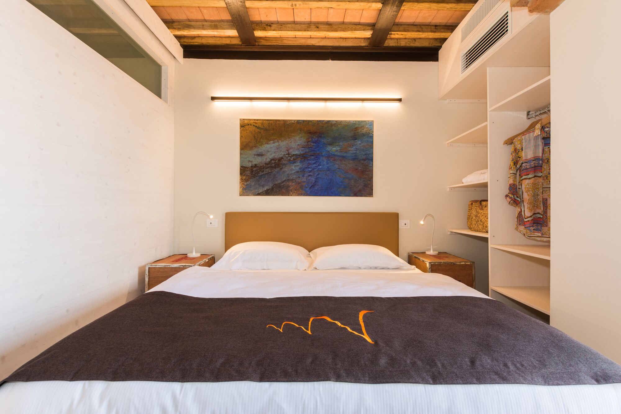 A bedroom with a bed, two bedside tables, a wall-mounted painting, and a built-in wardrobe.