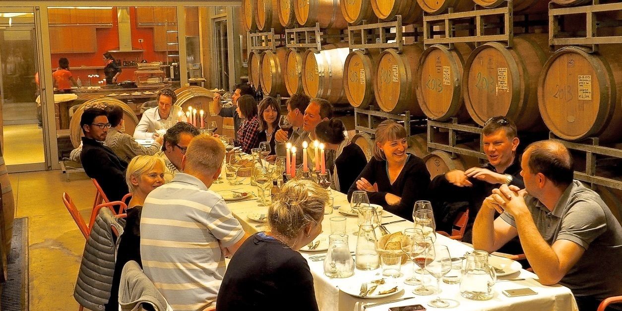 A group of people seated around a table in a room with wooden barrels on the wall.
