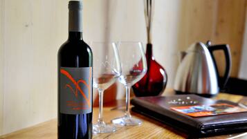 A wine bottle, two wine glasses, a red vase, and a black wallet on a wooden table.