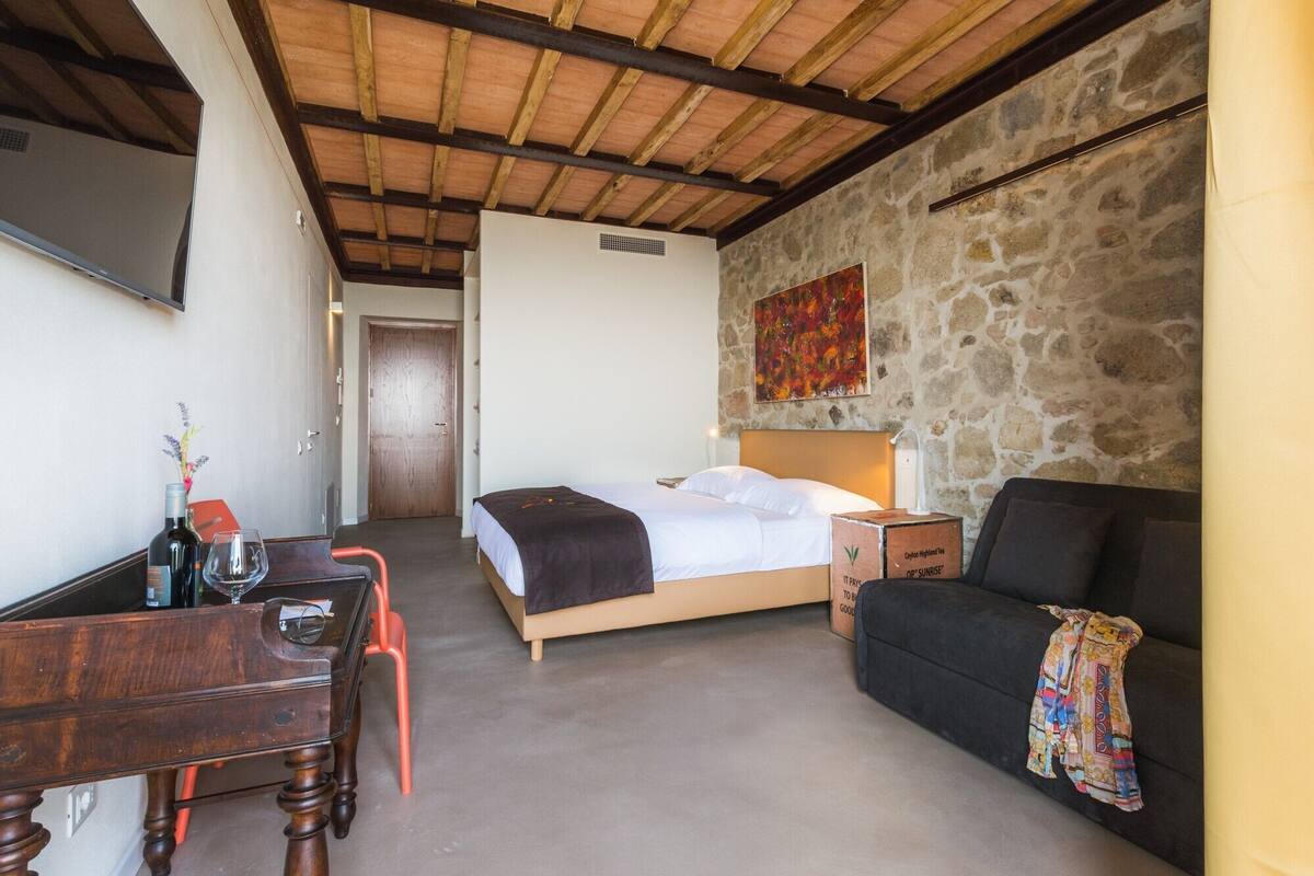 Un dormitorio con una cama, un escritorio, una silla, un sofá y una pared de piedra.