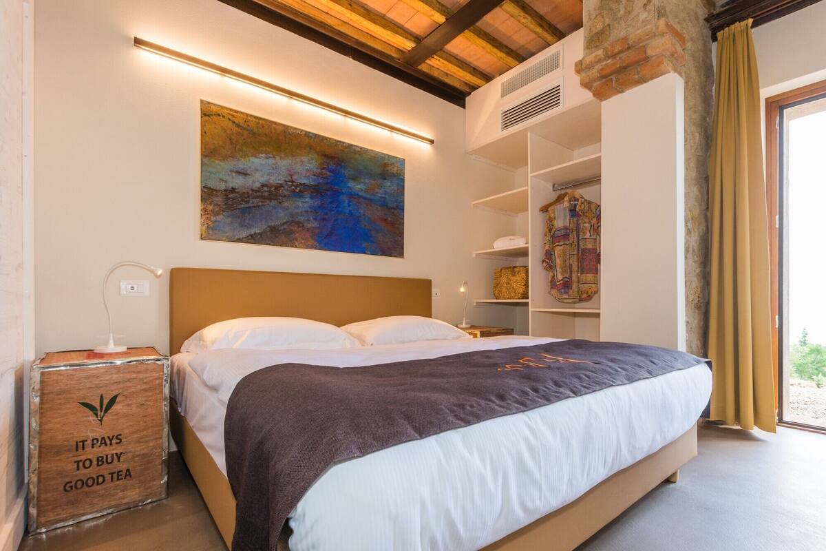Un dormitorio con una cama, un cuadro, una estantería con ropa y un cofre de madera con texto.