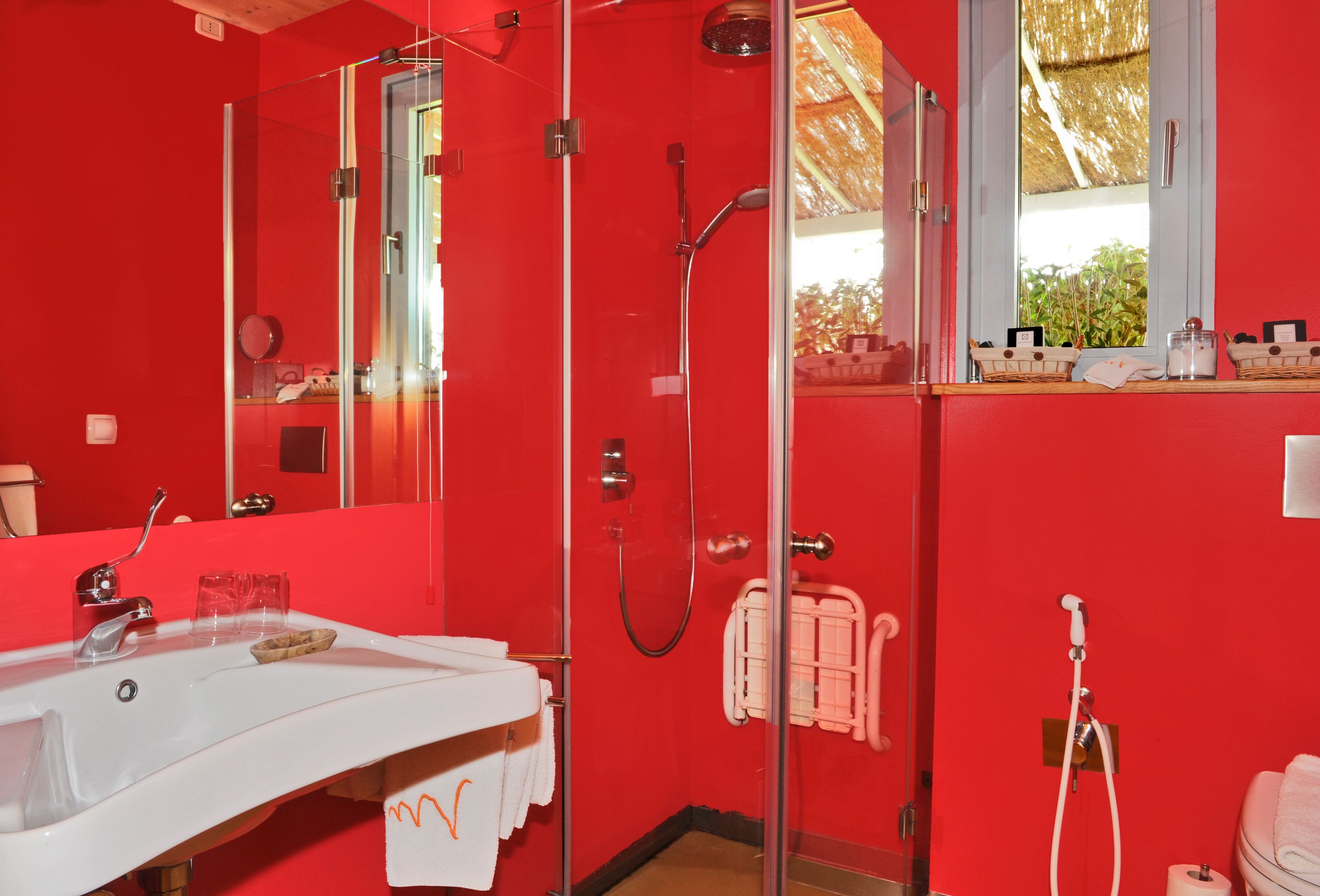 A red bathroom with a white sink, glass shower enclosure, and a window with a view of greenery.