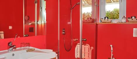 A red bathroom with a white sink, glass shower enclosure, and a window with a view of greenery.