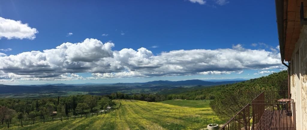 Un balcón con vista a un campo verde y montañas distantes bajo un cielo parcialmente nublado.