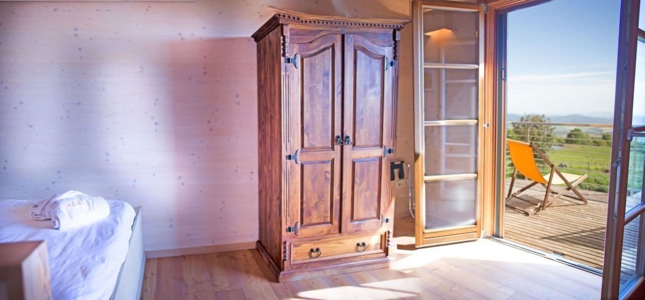 Een slaapkamer met een houten garderobe, een bed en een schuifglazen deur naar een balkon met een stoel.