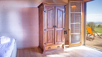 Een slaapkamer met een houten garderobe, een bed en een schuifglazen deur naar een balkon met een stoel.