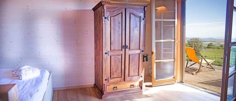 A bedroom with a wooden wardrobe, a bed, and a sliding glass door leading to a balcony with a chair.