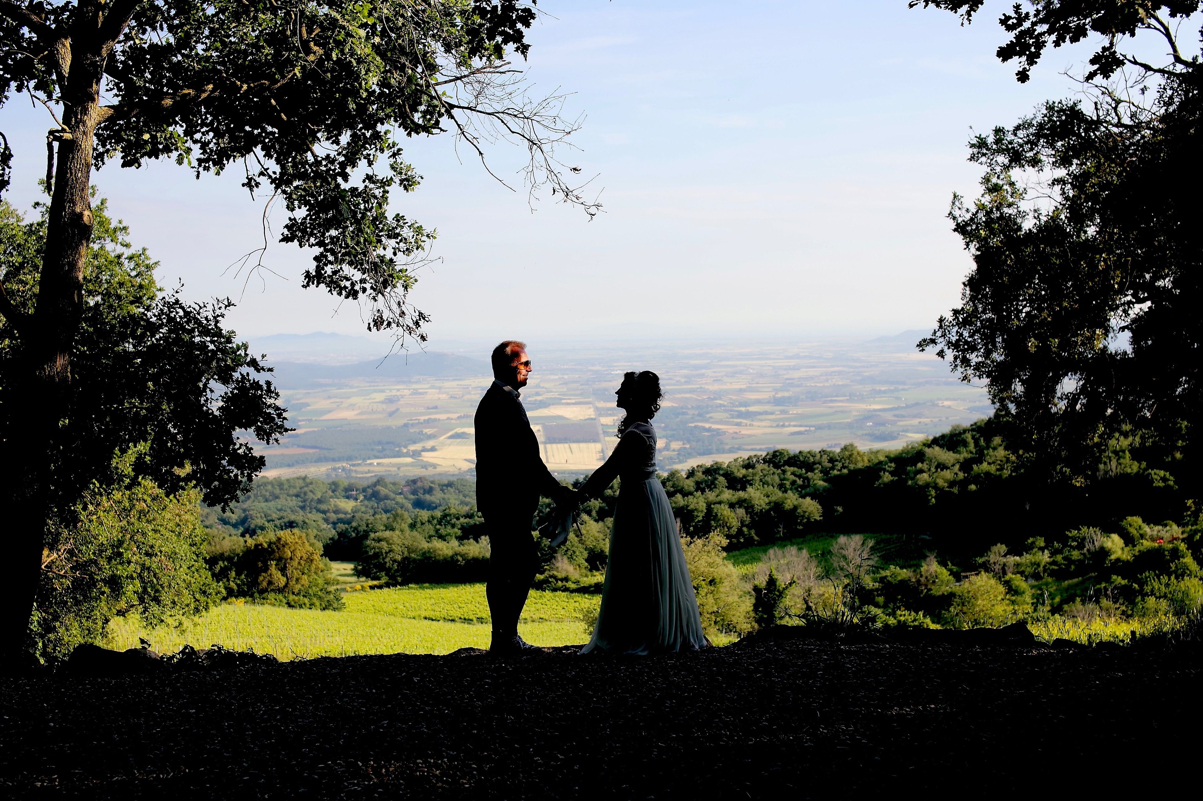 Un couple se tenant la main sur une colline, d’où l’on aperçoit une vallée, des arbres et un paysage lointain.