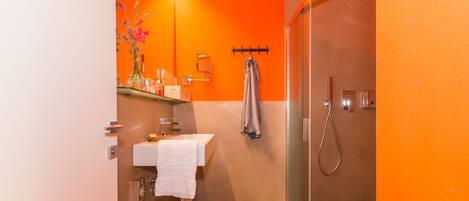 A bathroom with an orange wall, a white sink, a towel, and a shower.