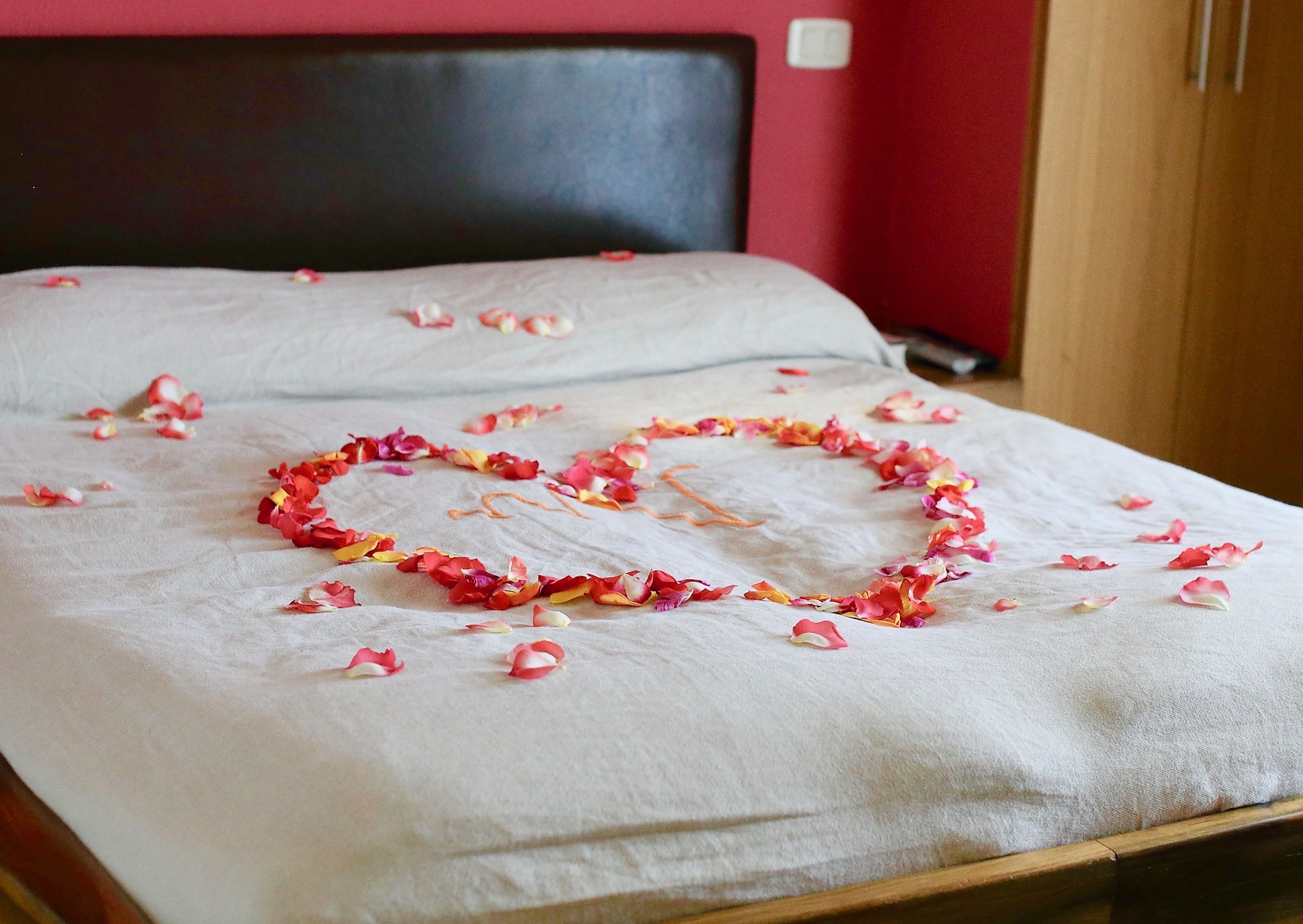A bed with a heart-shaped arrangement of rose petals on the bedspread.
