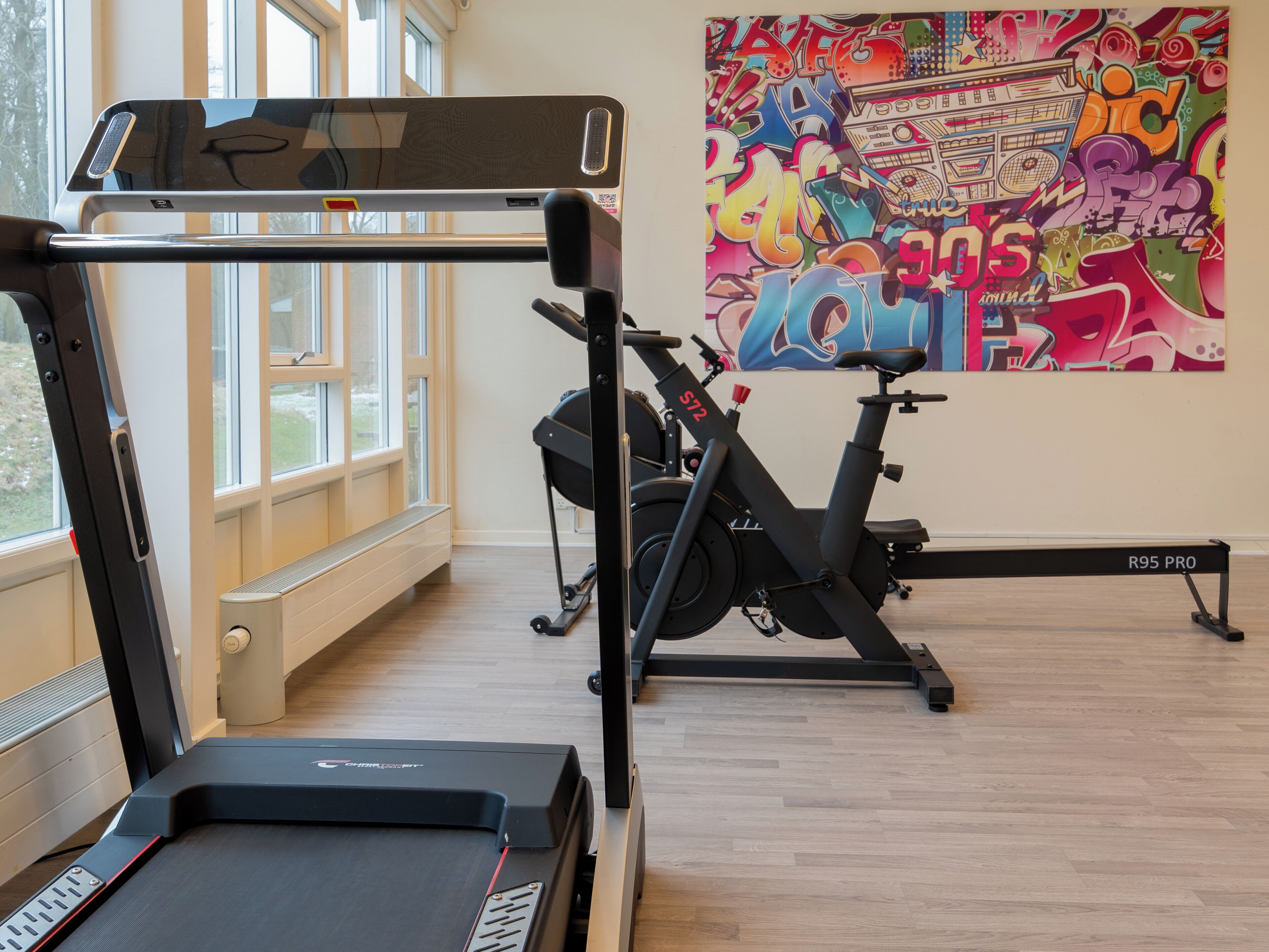 Ein Fitnessraum mit Trainingsgeräten, Laufband und einer Wand mit farbenfrohen Graffiti.