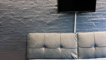 A grey tufted sofa against a textured brick wall with a mounted flat-screen TV above it.