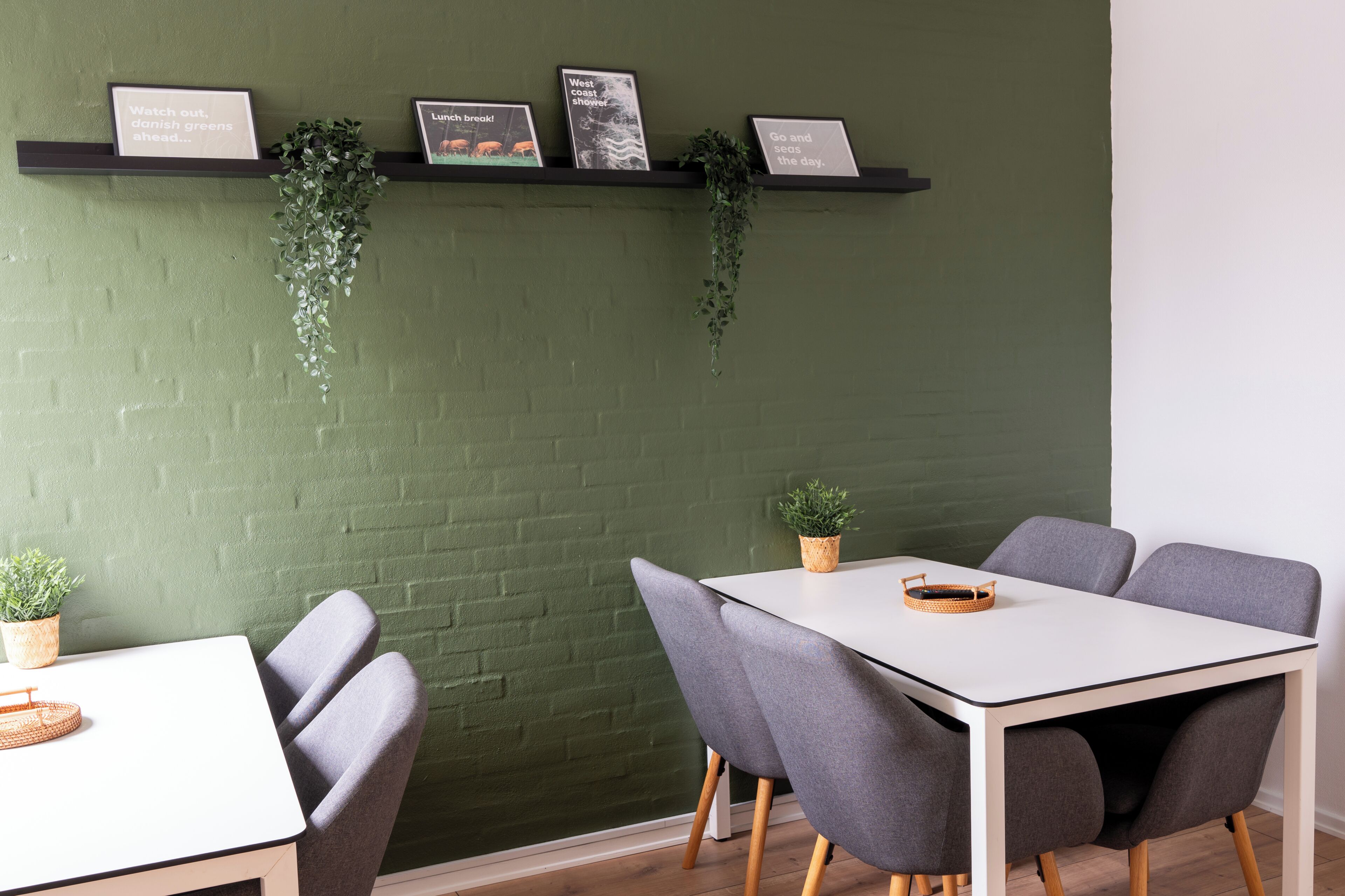 A dining area with a white table, grey chairs, and a green brick wall.