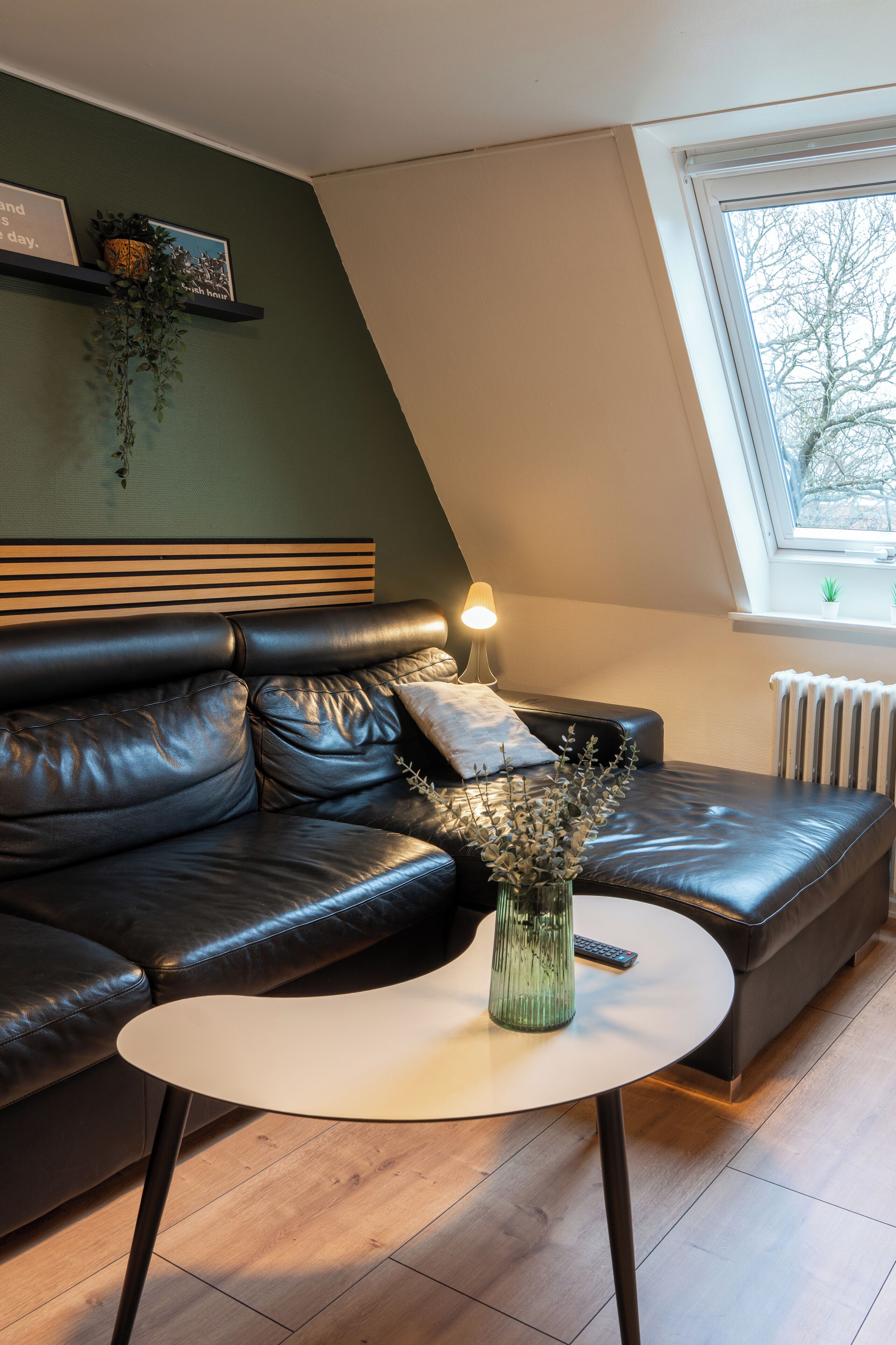 Un salon moderne avec un canapé en cuir, une table basse ronde, une lampe et une fenêtre donnant sur un beau paysage.