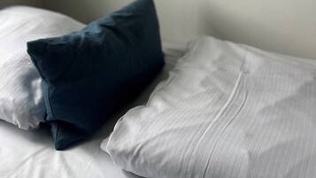 A bed with white linens and a dark blue pillow.