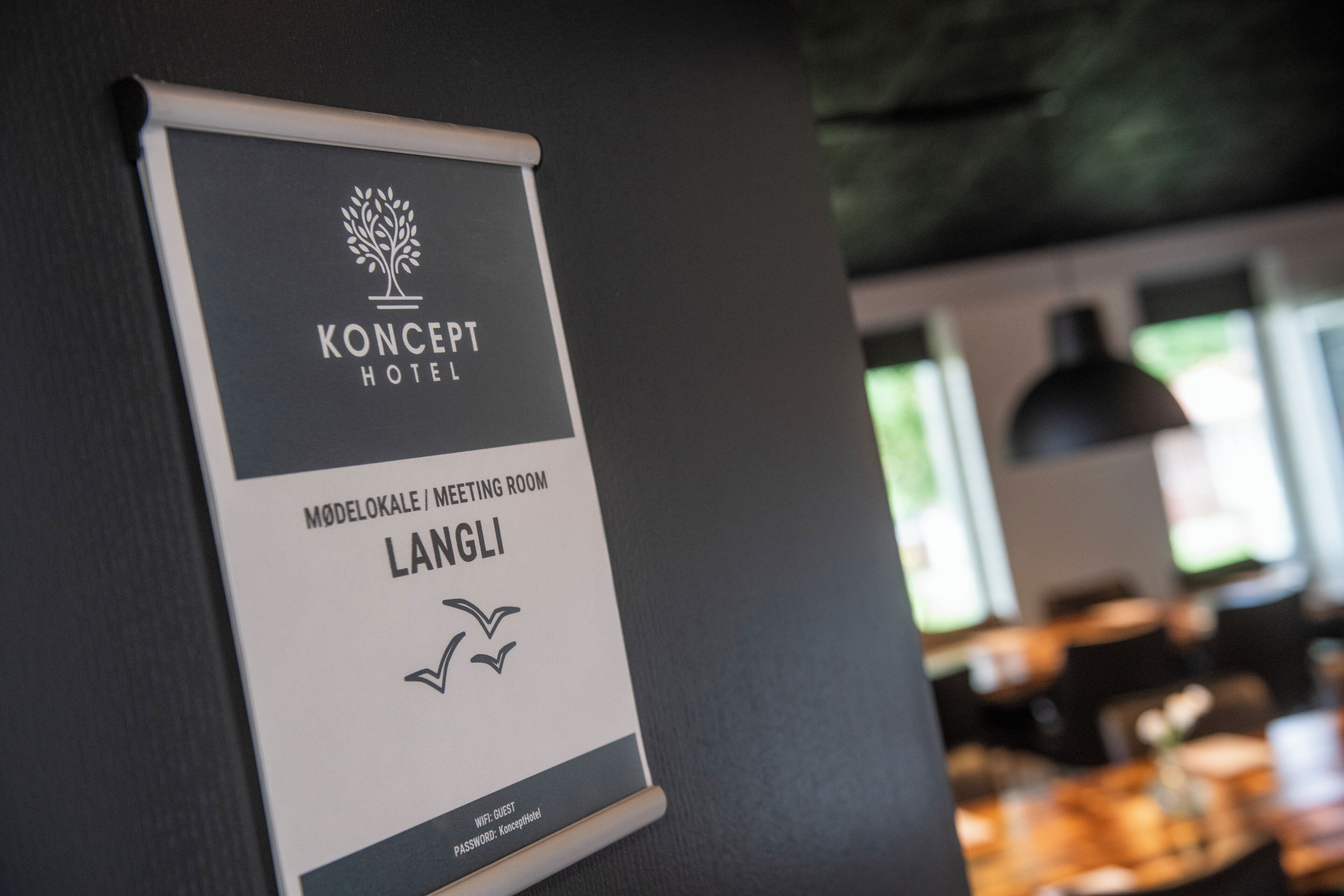 A sign for Koncept Hotel's meeting room, labeled 'MØDELOKALE / MEETING ROOM LANGLI' with a WiFi guest password.