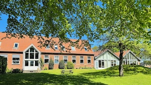 Een gebouw met een rood pannendak, grote ramen en een gazon met picknicktafels.