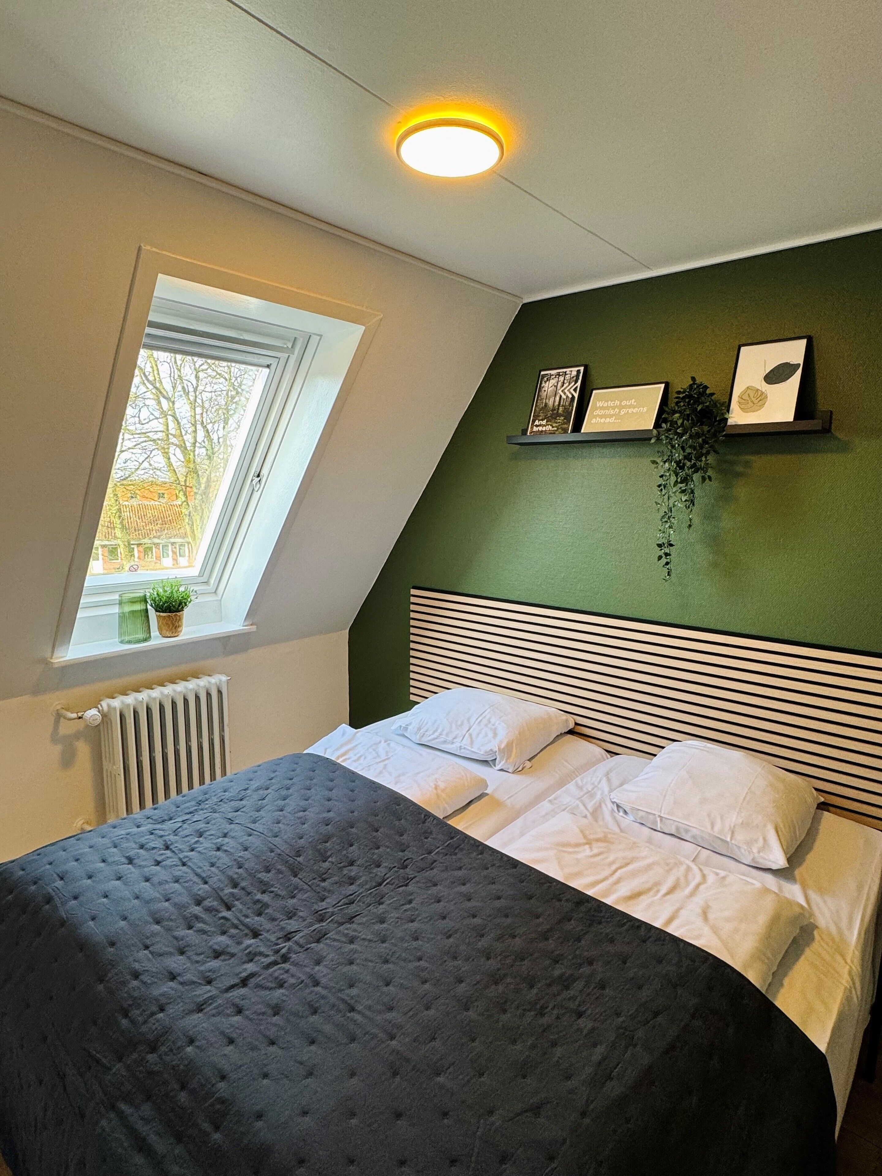 Quarto com cama, janela, radiador e parede verde com quadros.