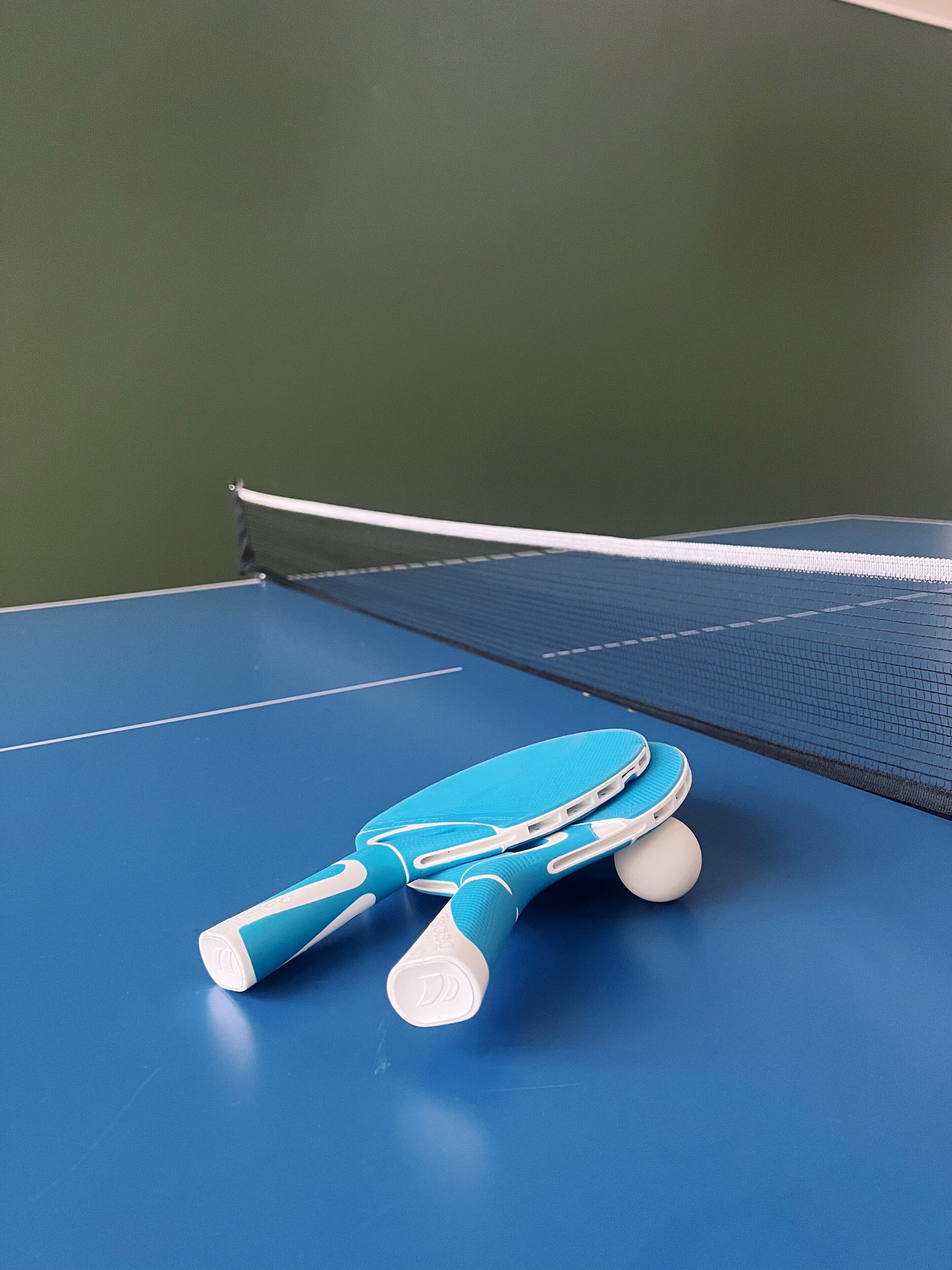 Una mesa de tenis de mesa azul con red en una habitación con paredes verdes.