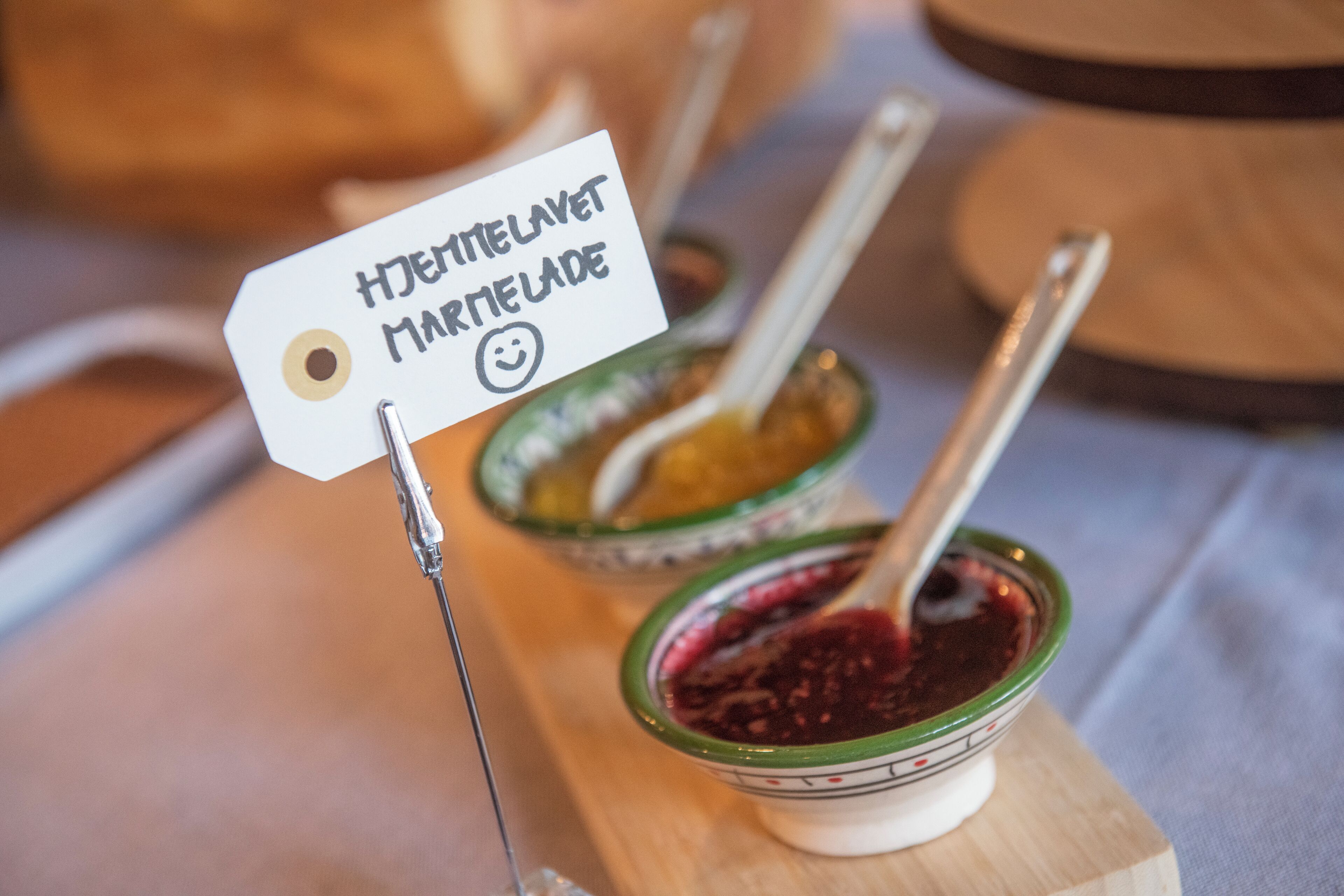 A wooden serving board with two bowls of jam, each with a spoon and a label.